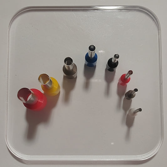A set of small hole punches arranged on a clear plastic tray against a white background.