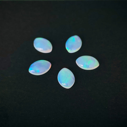 Five polished cabochon opal gemstones arranged in a loose circle on a solid black background, displaying a soft iridescent play-of-color with blue, green, and pink hues.