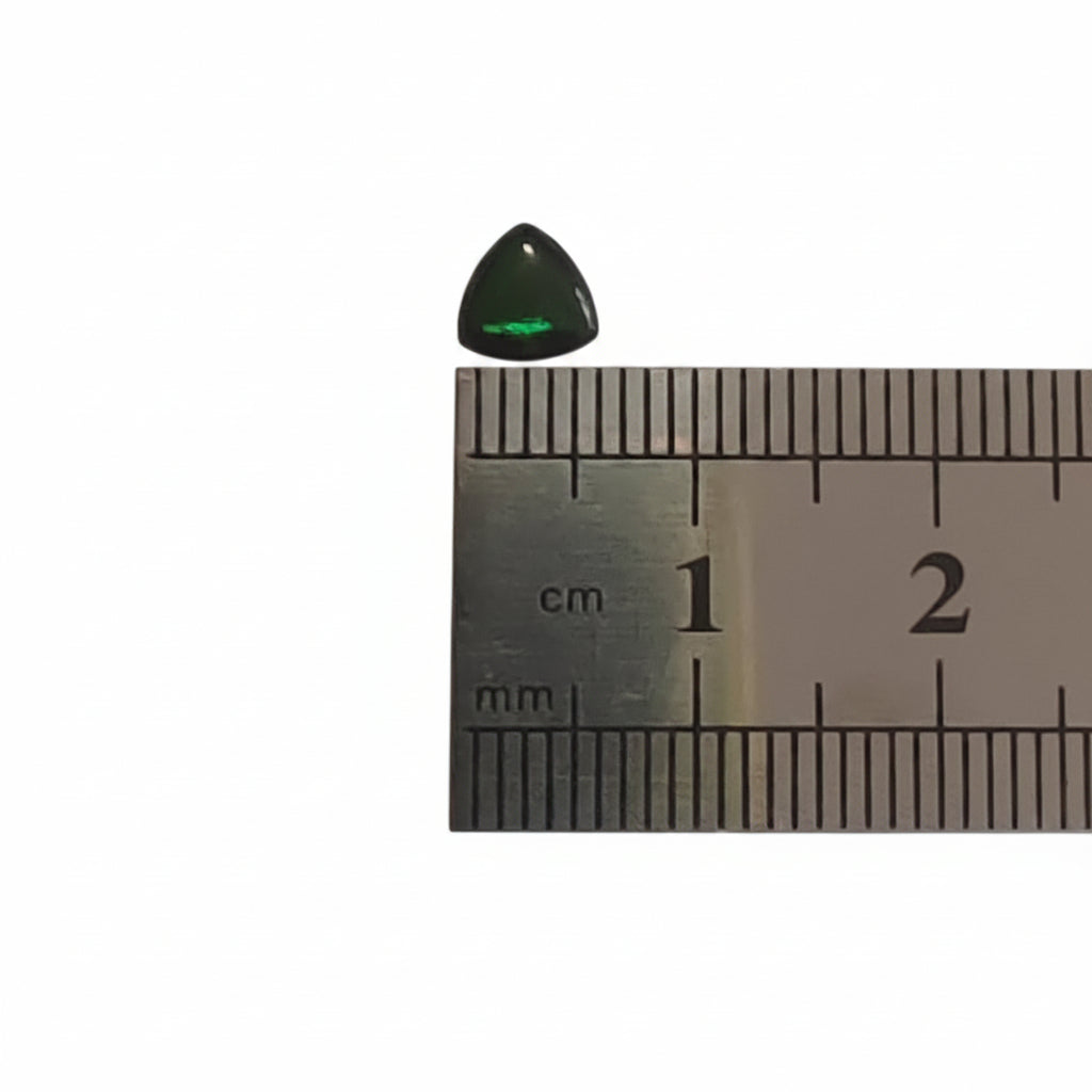 A small polished triangular dark green gemstone placed above a metal ruler for size reference on a plain light background.