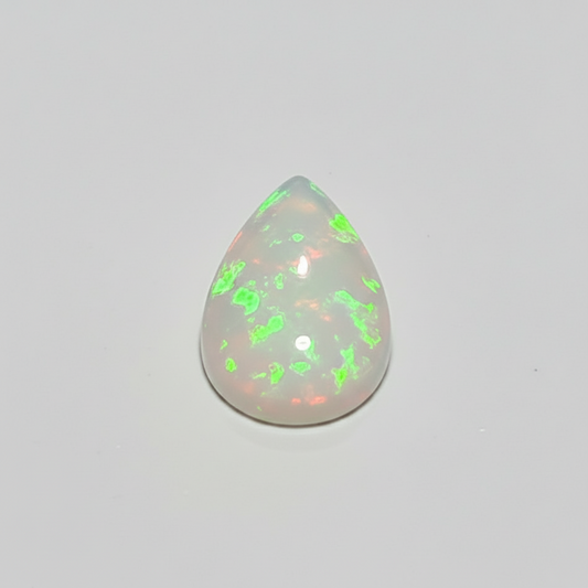 A teardrop-shaped cabochon gemstone with a milky white base and vibrant, shifting internal flashes of neon green and coral pink, set against a plain light grey background.