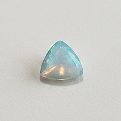A small triangular cabochon gemstone with iridescent blue, green, and white opalescent play-of-color, set against a plain light gray background.