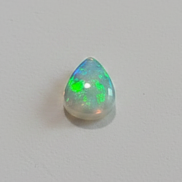 A small teardrop-shaped opal gemstone with a vibrant green and blue play-of-color, displayed on a plain light gray surface.