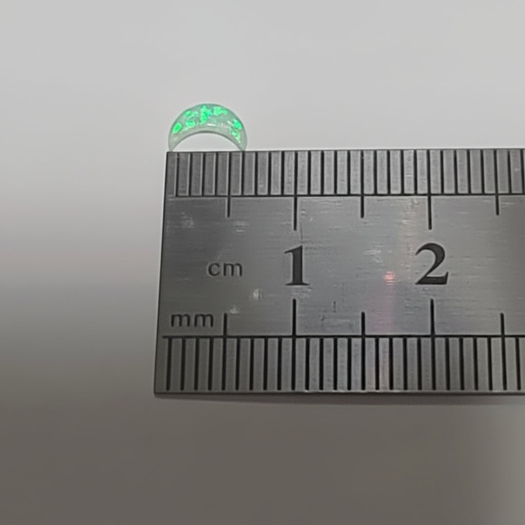 A small iridescent moon shaped opal shown next to a metal ruler with centimetre markings to indicate its size.