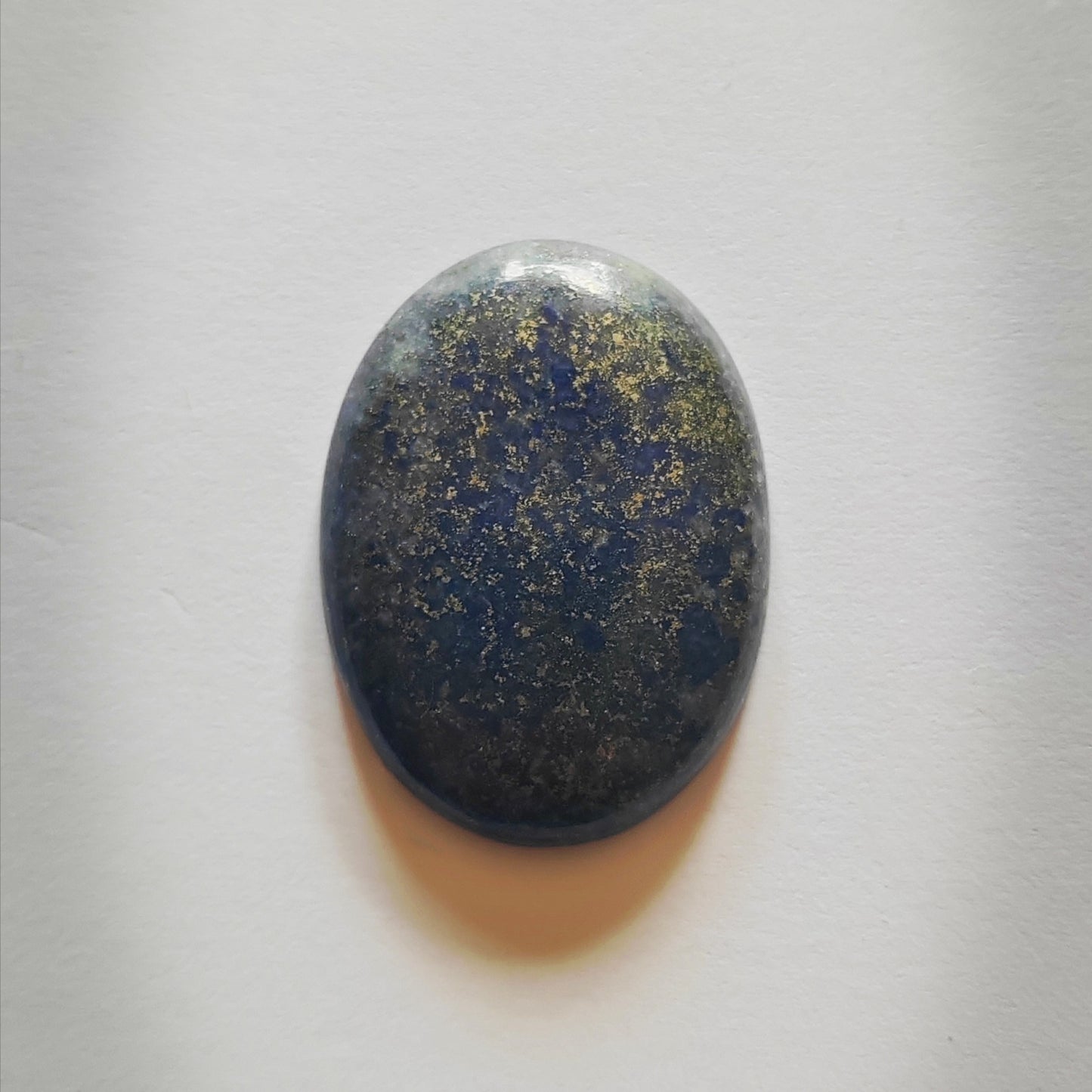 Oval-shaped stone with a blue and gold speckled pattern on a white background