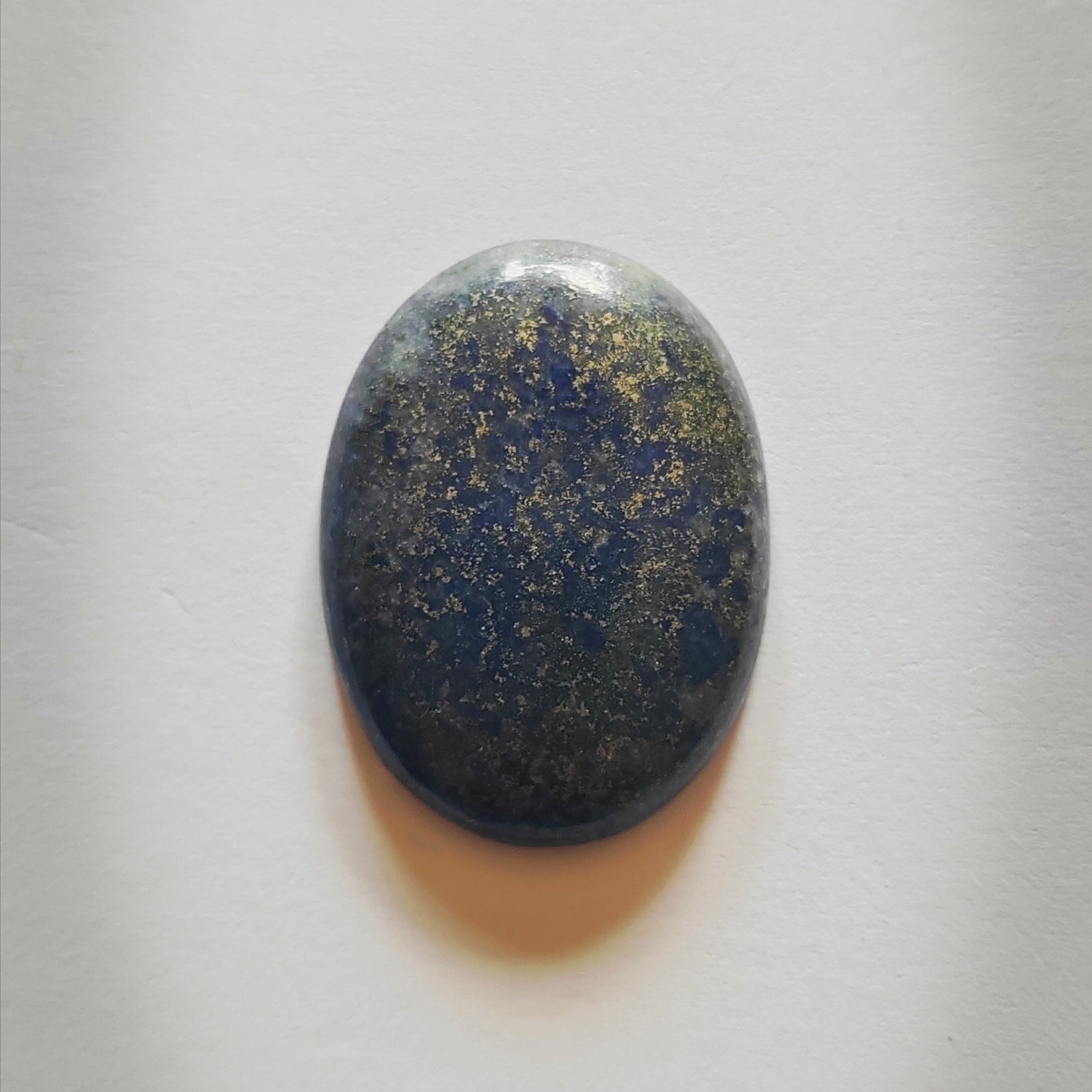 Oval-shaped stone with a blue and gold speckled pattern on a white background
