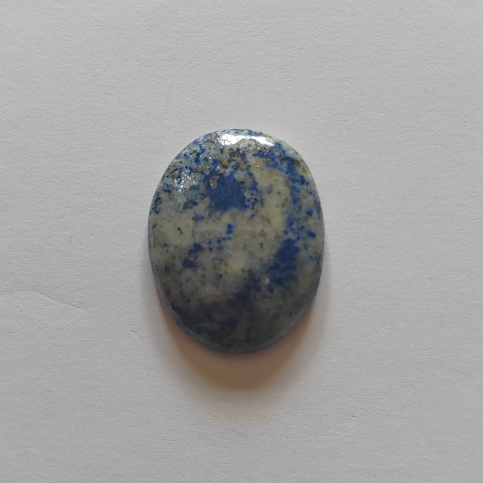 Oval-shaped stone with blue and white speckled pattern on a light gray background