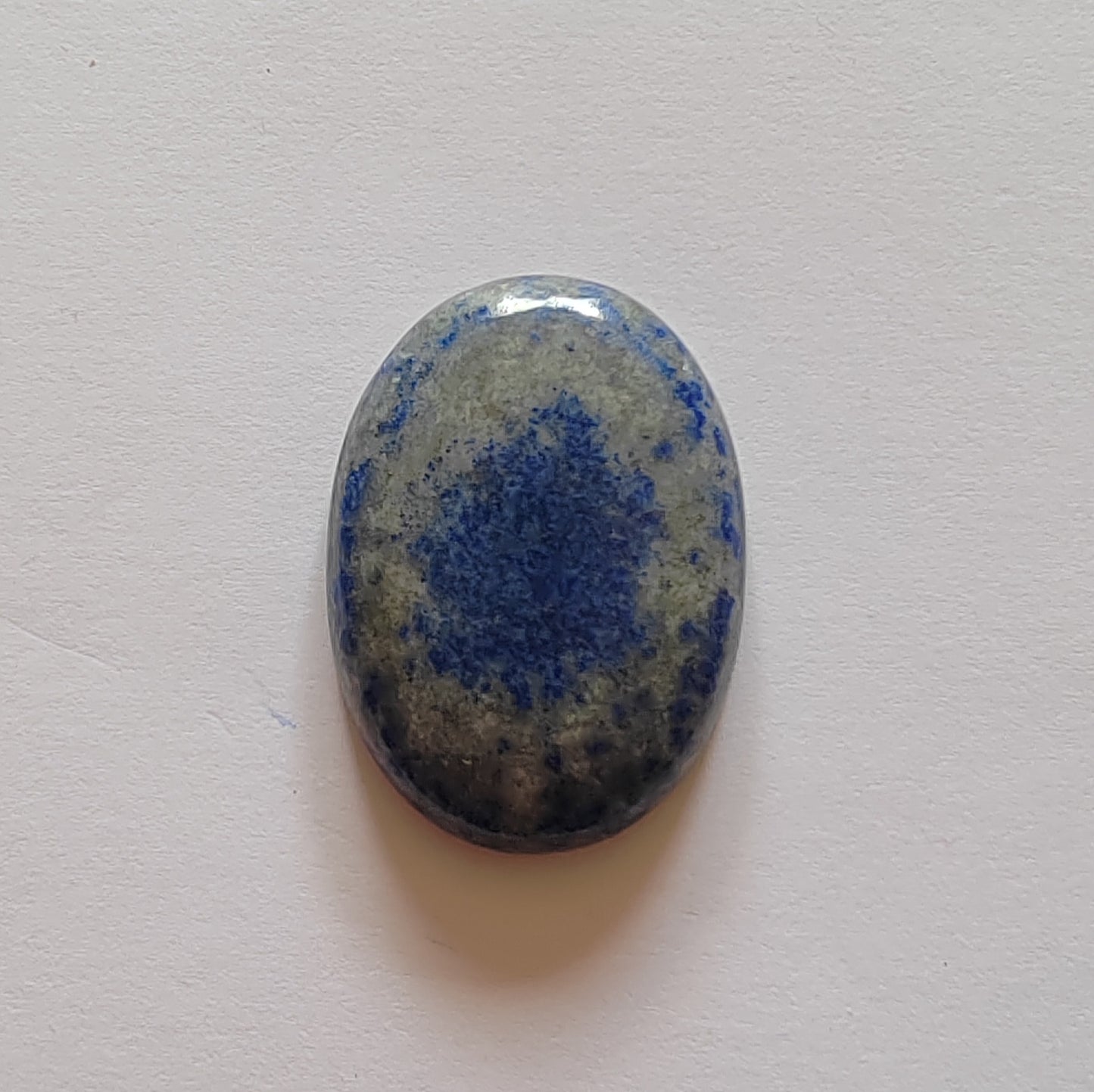 Oval-shaped stone with blue speckled pattern on a light grey background