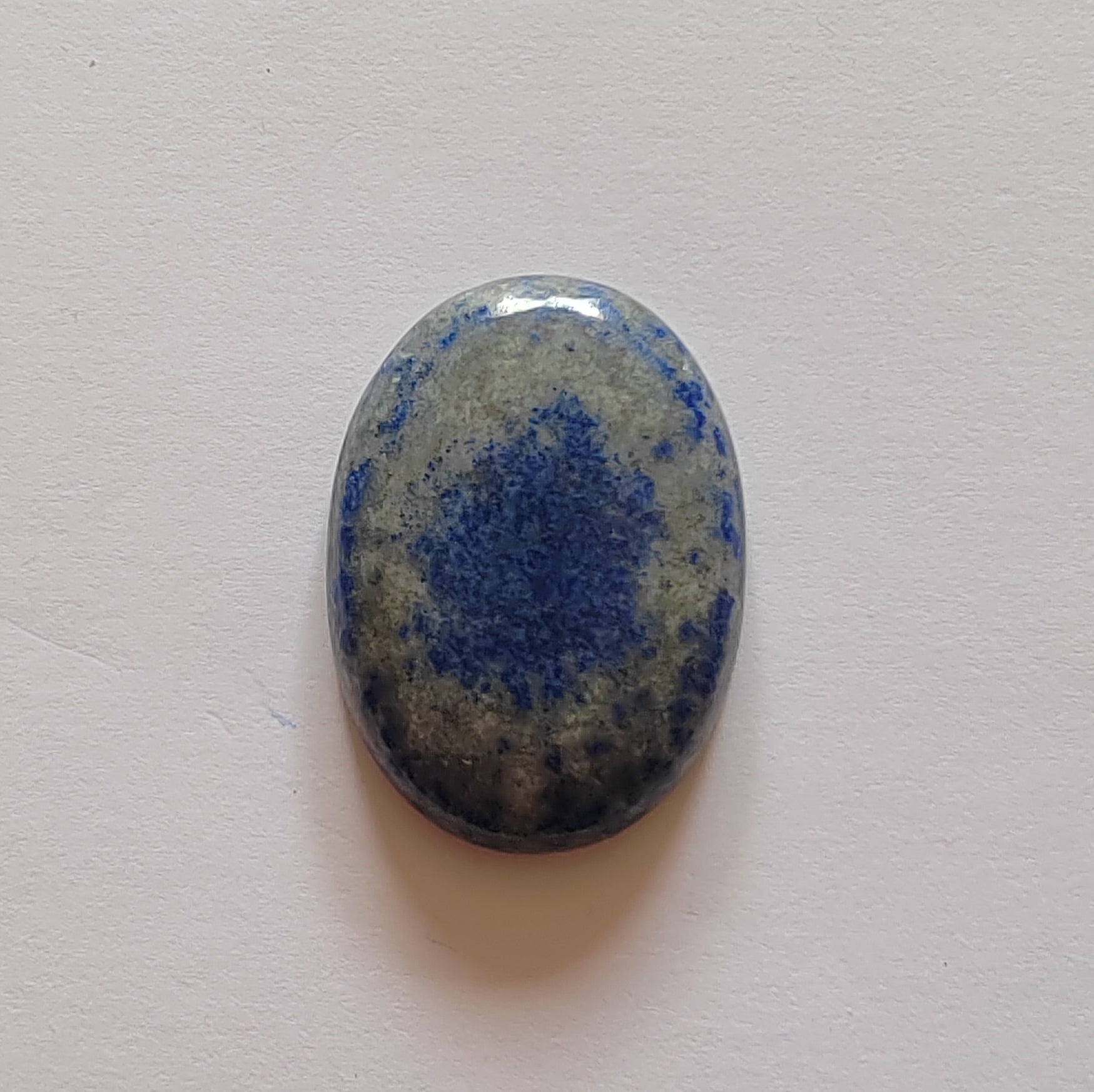 Oval-shaped stone with blue speckled pattern on a light grey background