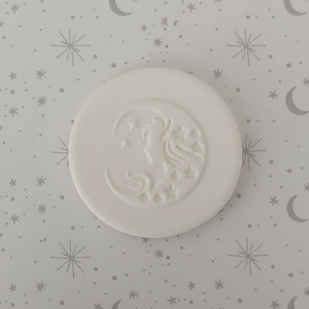 A round clay stamp featuring an embossed crescent moon and star design.