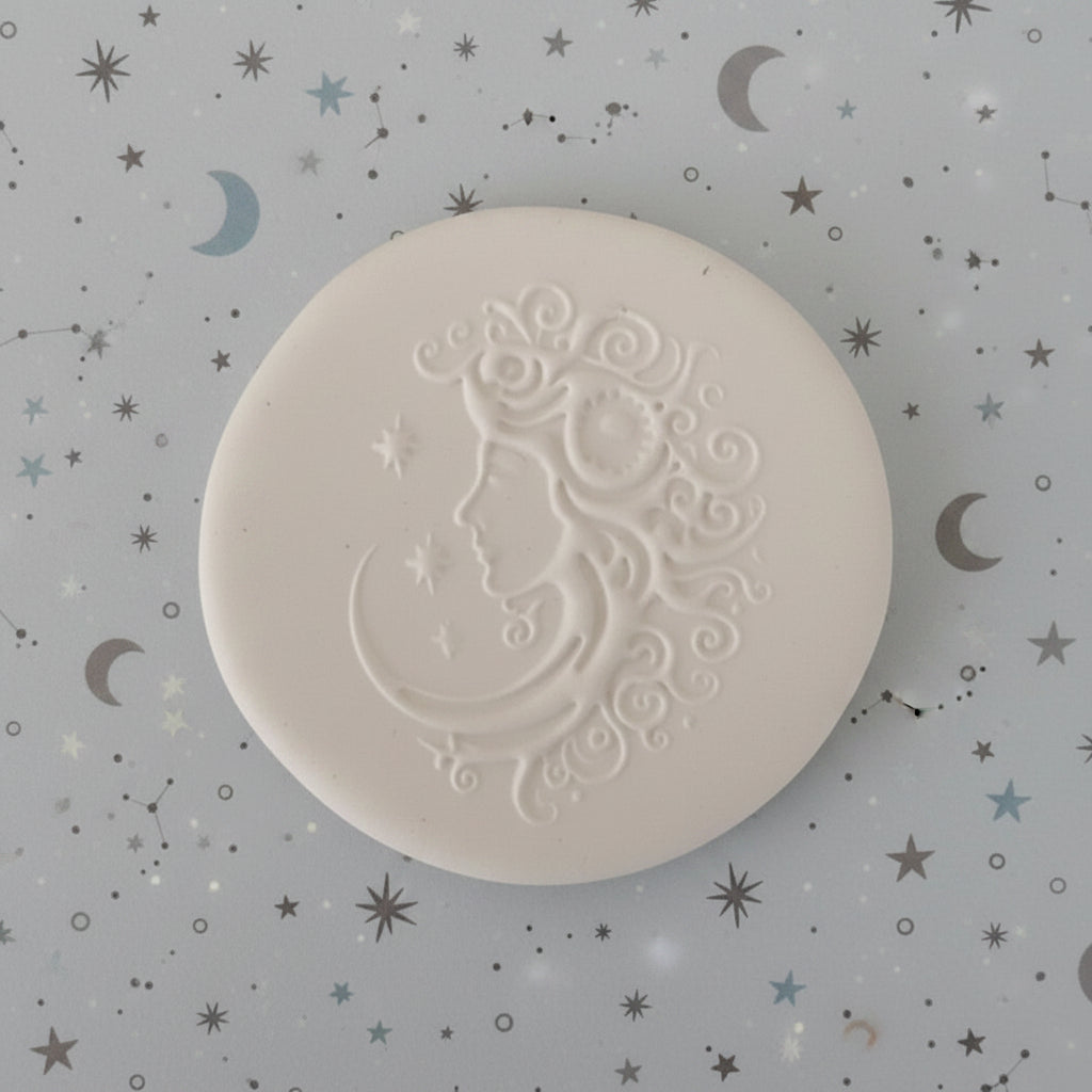 A round clay embossed profile of a woman's face next to a crescent moon and stars.