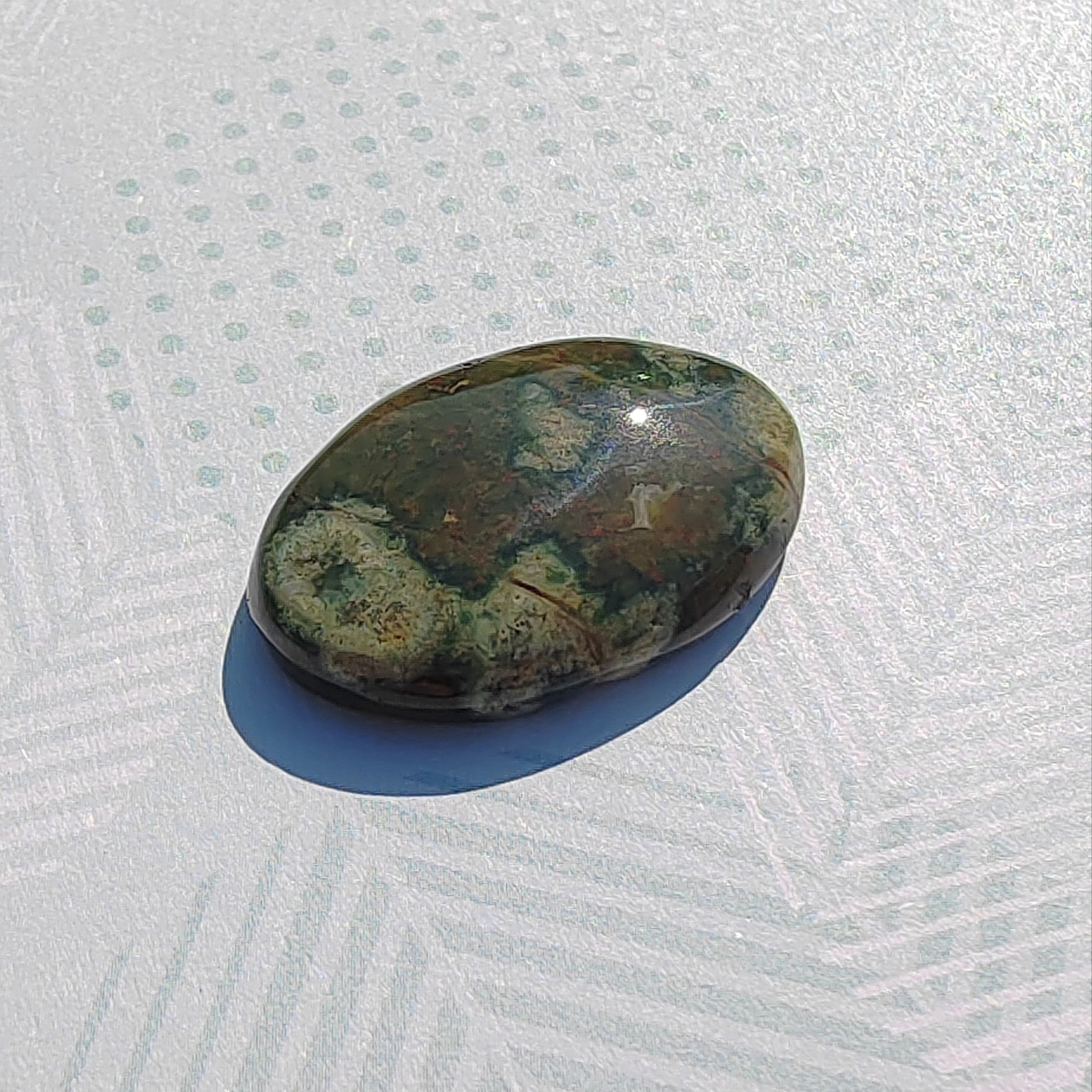 Oval-shaped green and brown stone on a textured white surface