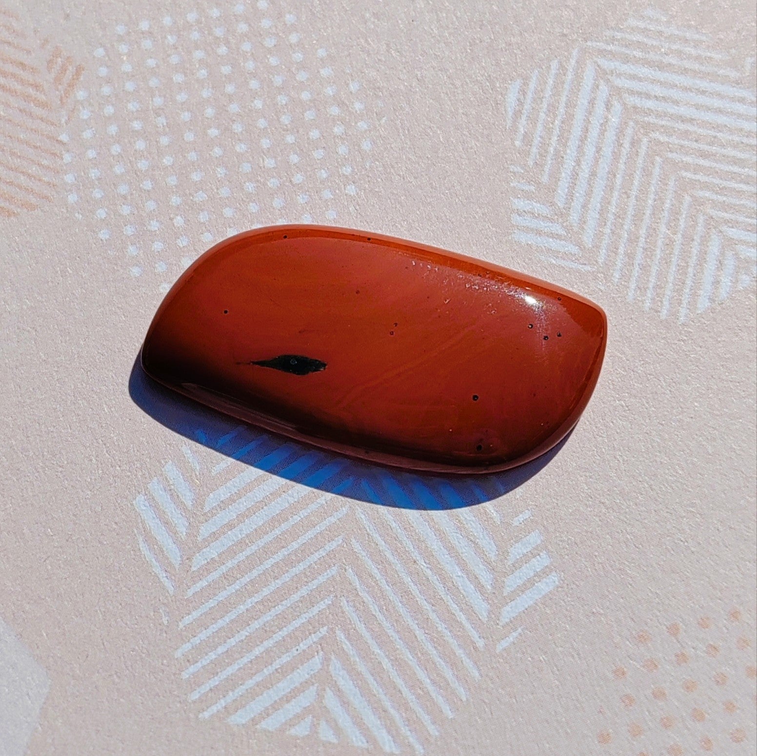 A red jasper irregular flat backed cabochon with specks of black.