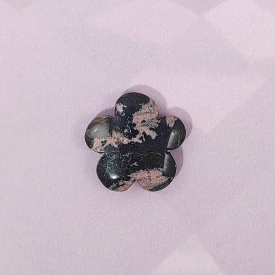 Flower-shaped stone with black and pink patterns on a light purple background