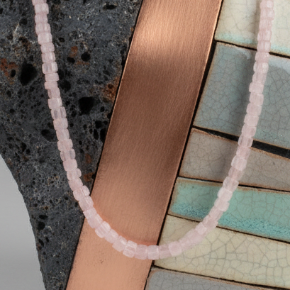 Necklace with pink beads on a wrist against a textured surface