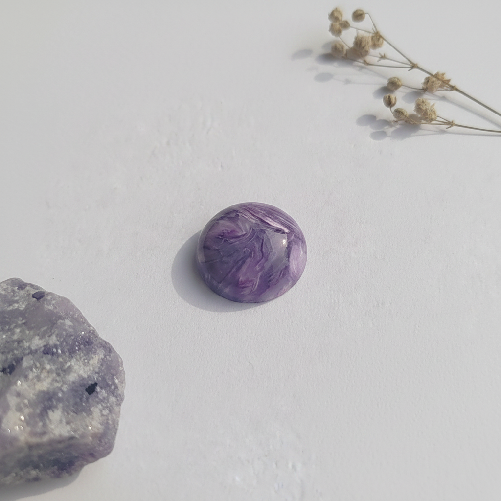 Purple charoite on a light background with dried flowers.