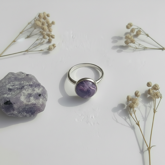Silver ring with a purple gemstone on a white surface with dried flowers and a rock.