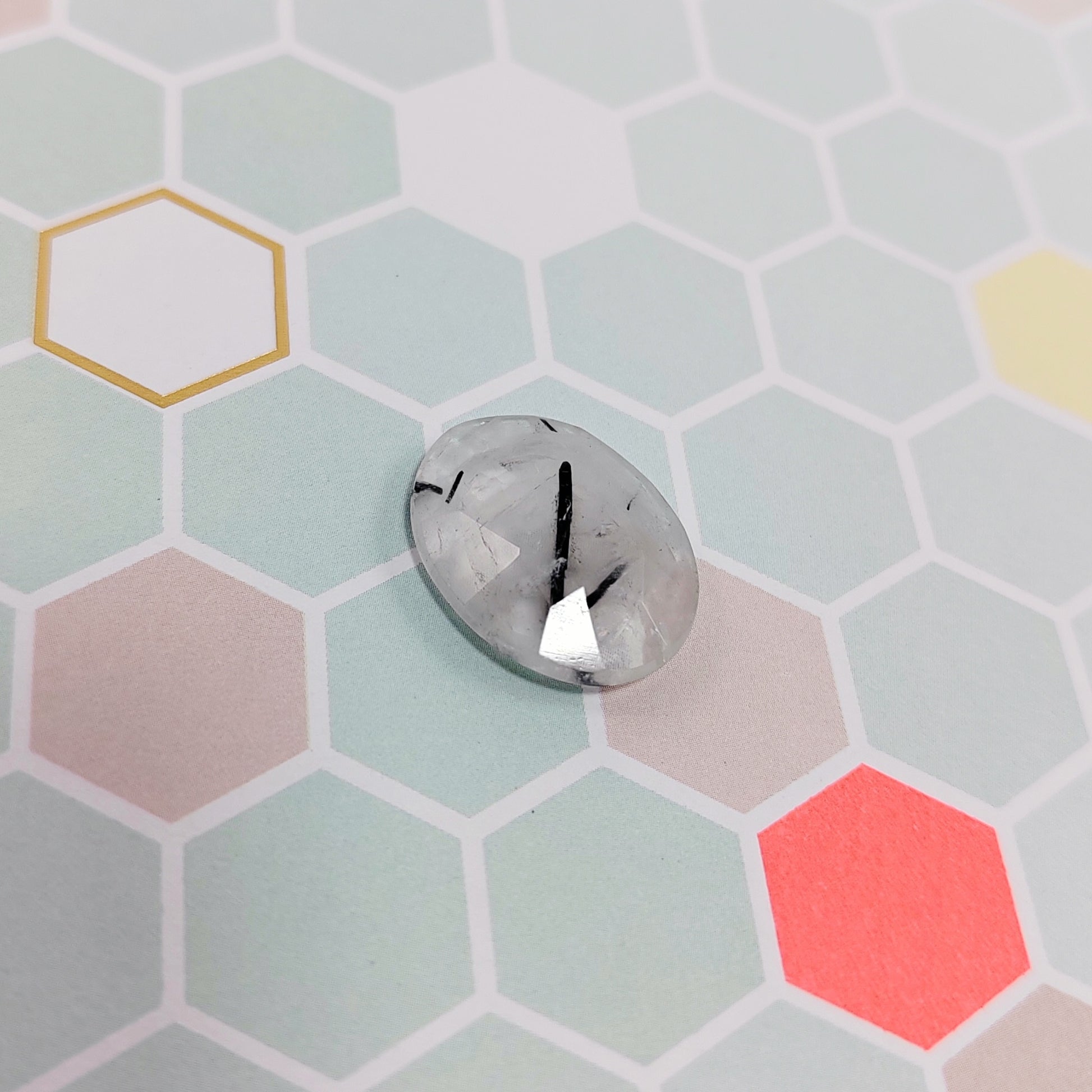 Hexagonal tile with a rutilated quartz on a multi-coloured hexagonal tile background