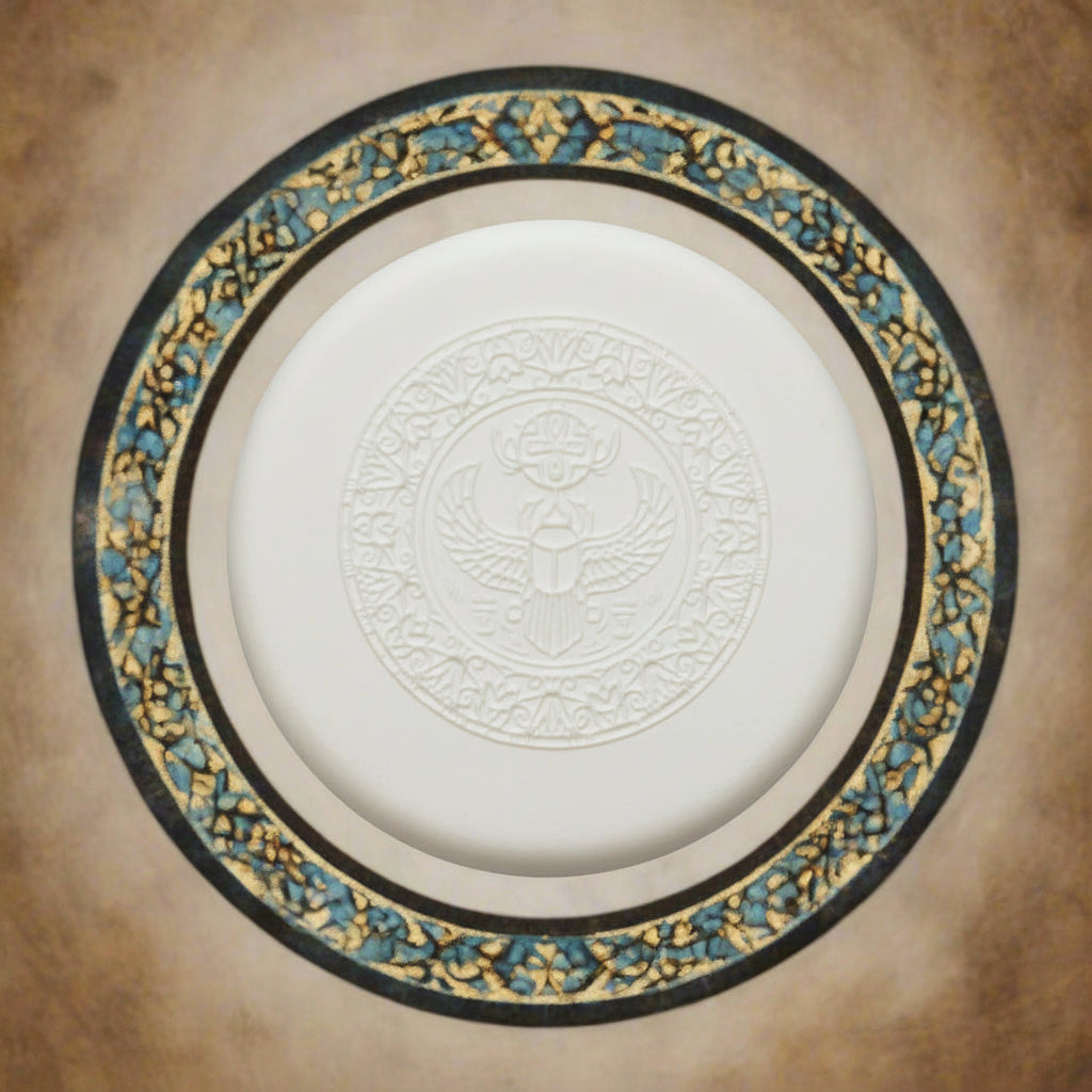 A round clay embossed Egyptian scarab beetle design, cantered on a decorative circular plate with gold, blue, and black patterns against a textured beige background.