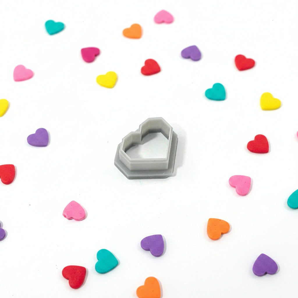 Heart-shaped cutter surrounded by colourful heart-shaped candies on a white background