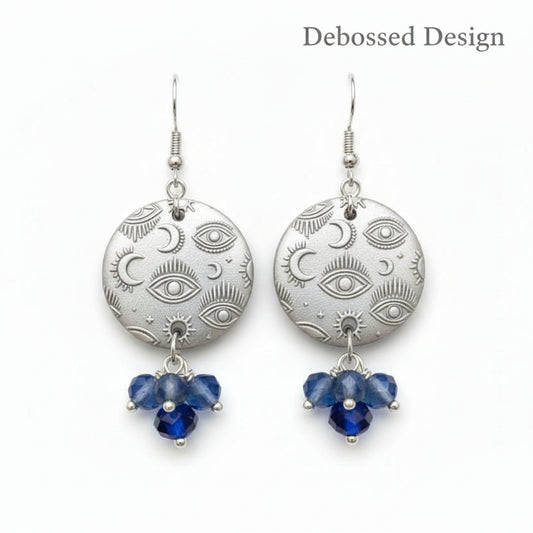 A small mystical eye repeat pattern embossed In silver dangly earrings with beads.