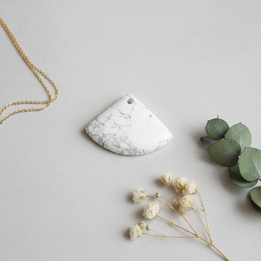 Marble-patterned pendant on a gold chain with green leaves and white flowers on a light gray background