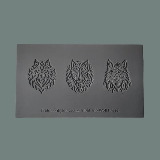 A dark grey rectangular texture mat with three embossed tribal wolf head designs, displayed on a textured white fabric background.