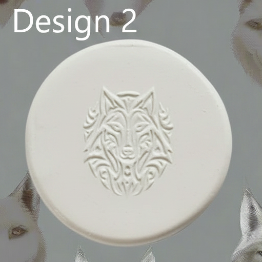 A round white clay with an embossed wolf head design, shown against a grey background with partial white feather-like elements at the sides and the text 'Design 2' at the top.