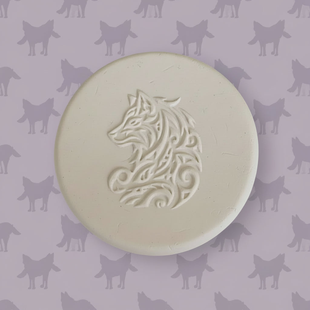 A round clay embossed wolf design embossed in clay, using a rubber texture mat called sitting wolf designs.