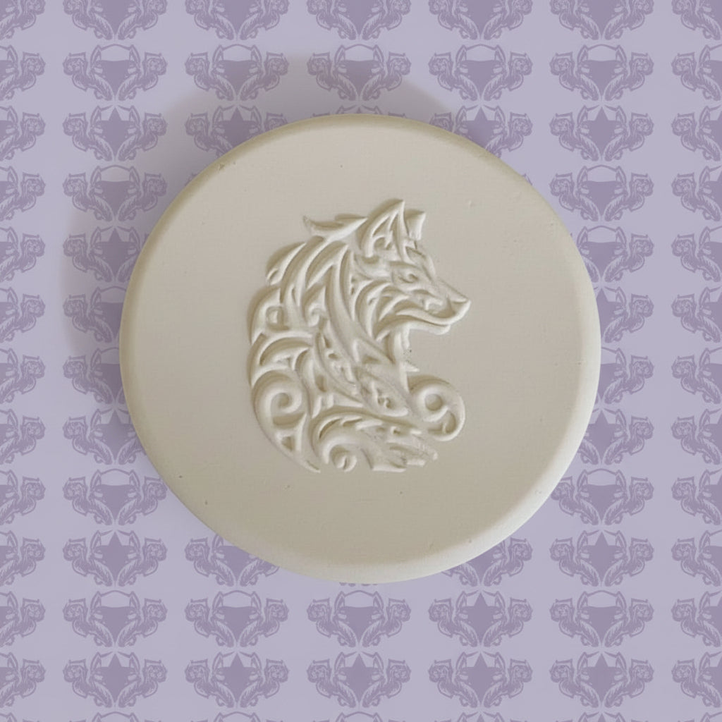 A round clay embossed wolf design embossed in clay, using a rubber texture mat called sitting wolf designs.