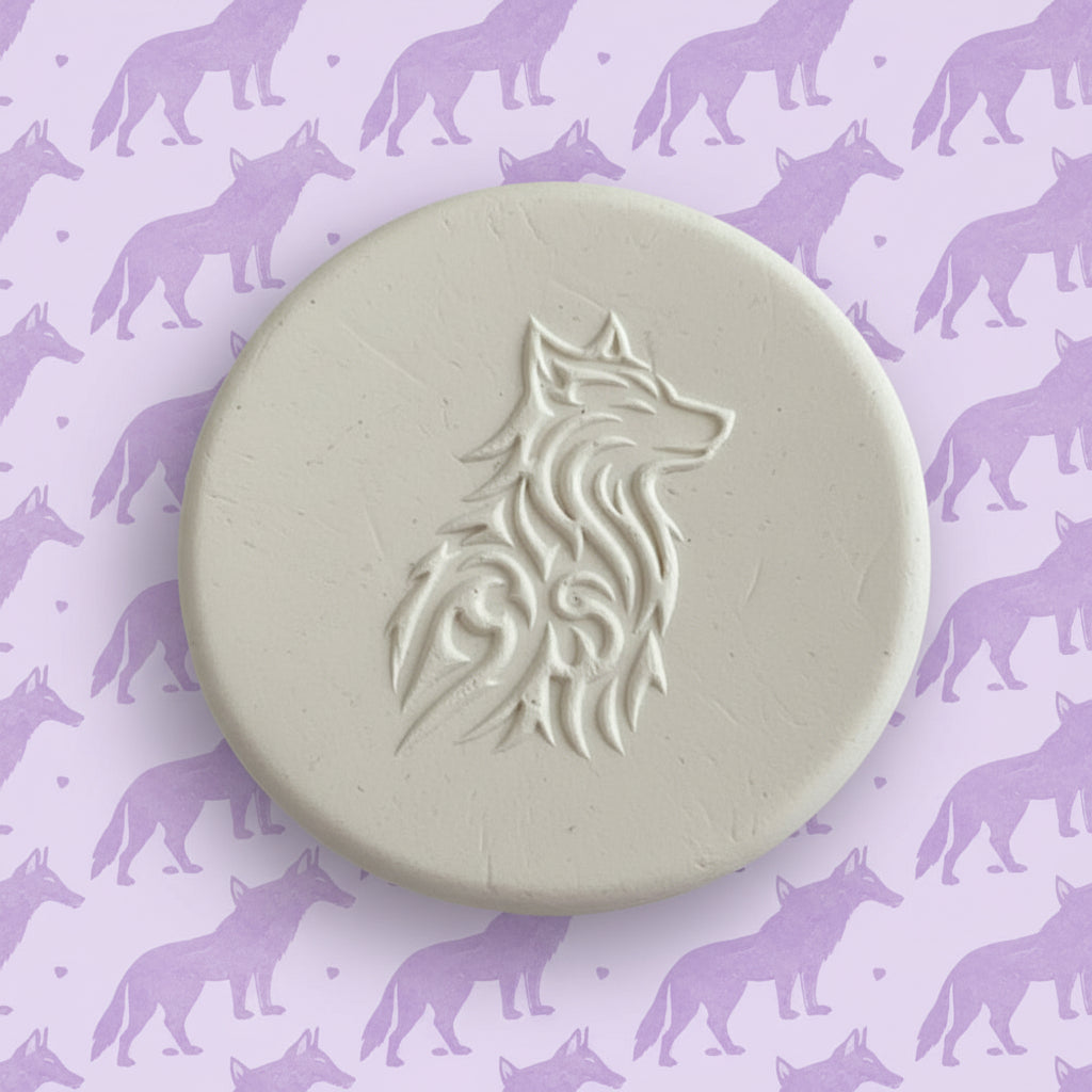 A round clay embossed wolf design embossed in clay, using a rubber texture mat called sitting wolf designs.