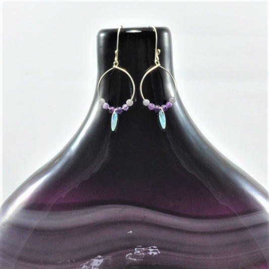 Bohemian hoop earrings featuring semi-precious amethyst beads on French hook earwire with ball detail crafted in 925 sterling silver. Amethyst beads display shades of lavender and purple, with a frosty lilac accent drop bead. Each earring weighs 1.5g ensuring a comfortable fit.