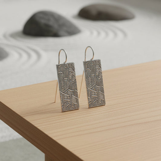 Pair of silver earrings with bamboo geometric pattern on a zen background