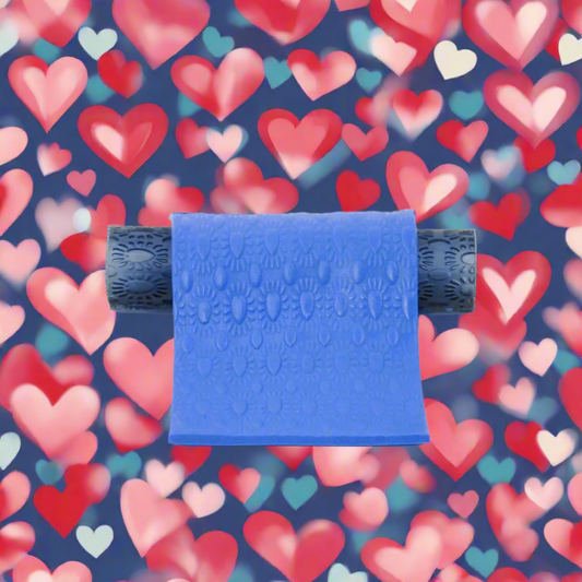A blue textured roller capulet with a heart pattern in the background, used for crafting with clay.