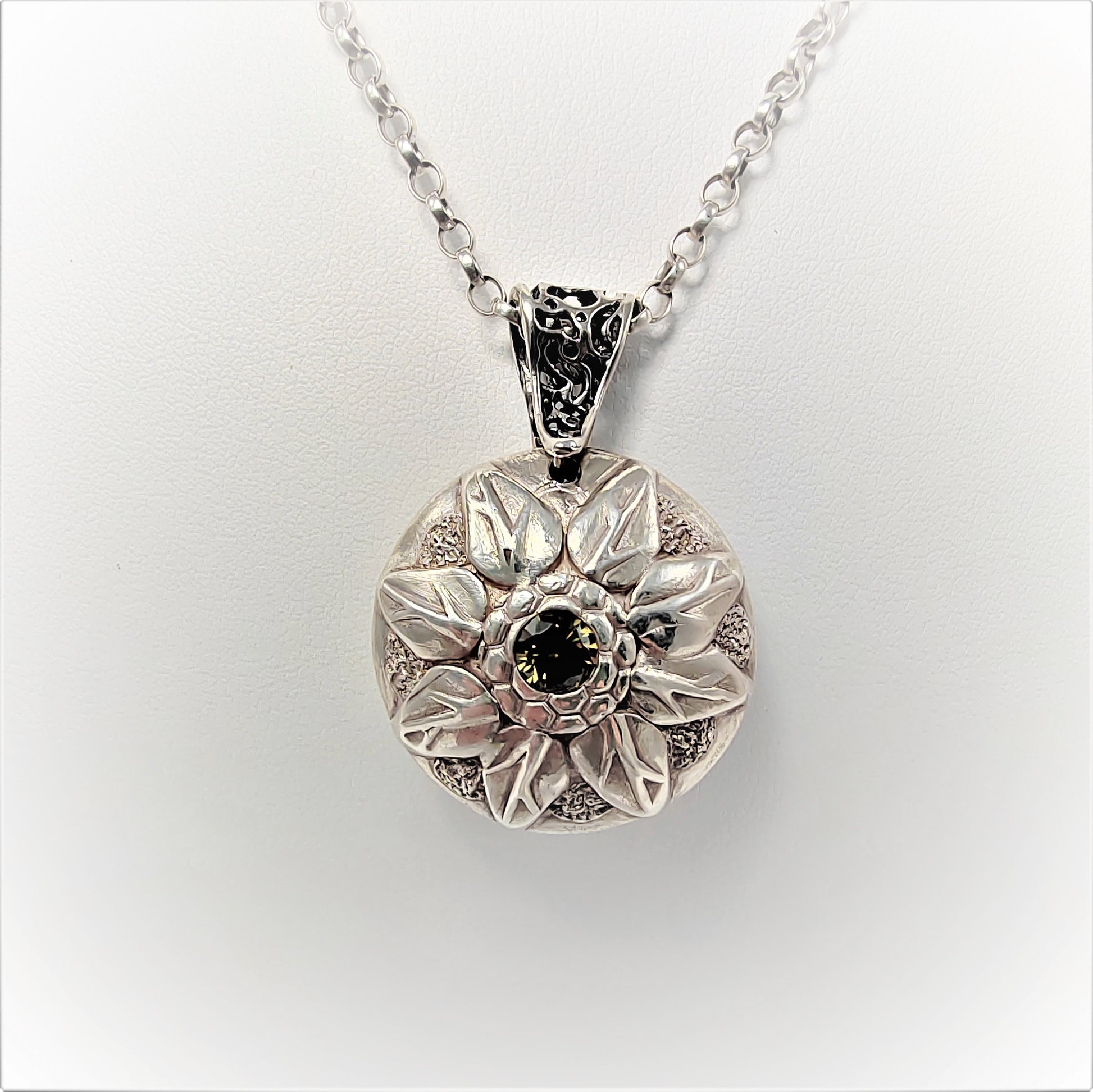 This 999 fine silver lentil bead pendant is double-sided: one features a daisy flower with a central amethyst cubic zirconia, and the other an 8-pointed flower centered on an olive cubic zirconia. It comes with a trace chain and is stamped with a London hallmark beneath the bail.  