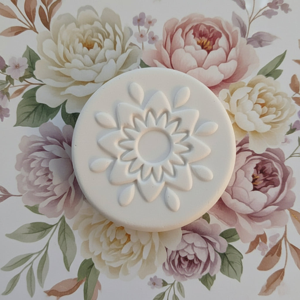 A small  clay stamp with a raised flower-like embossed pattern, shown on a flowery background.