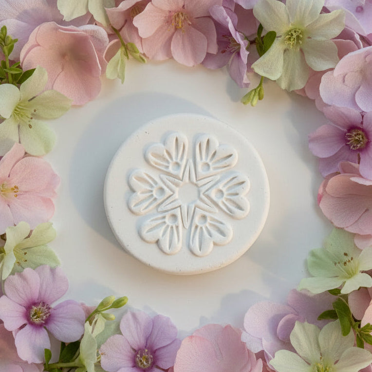 A round clay stamp with a floral snowflake design, shown on a light gray surface.