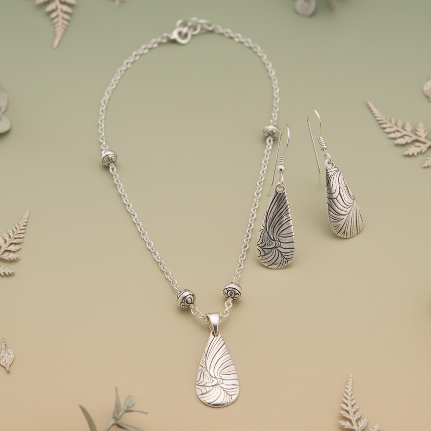 Silver necklace and earrings on a light green background with leaf decorations