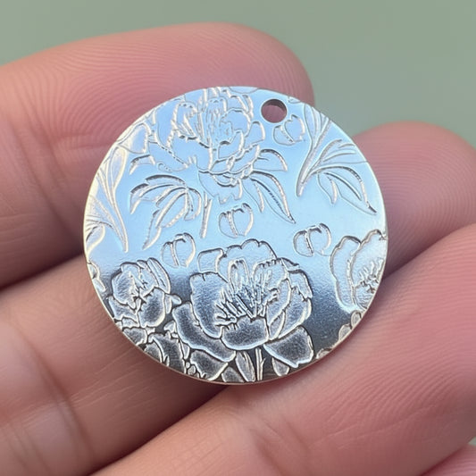 Silver floral pendant held between fingers with a blurred background