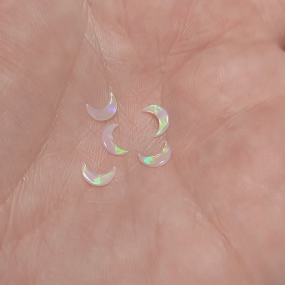 Five moon shaped fireable opals displaying the flash of green fire on a hand.