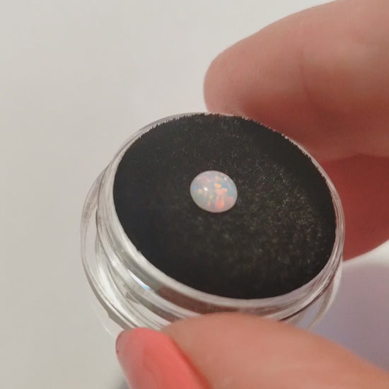 A pink opal cabochon on a jewellery cushion showing red flashes