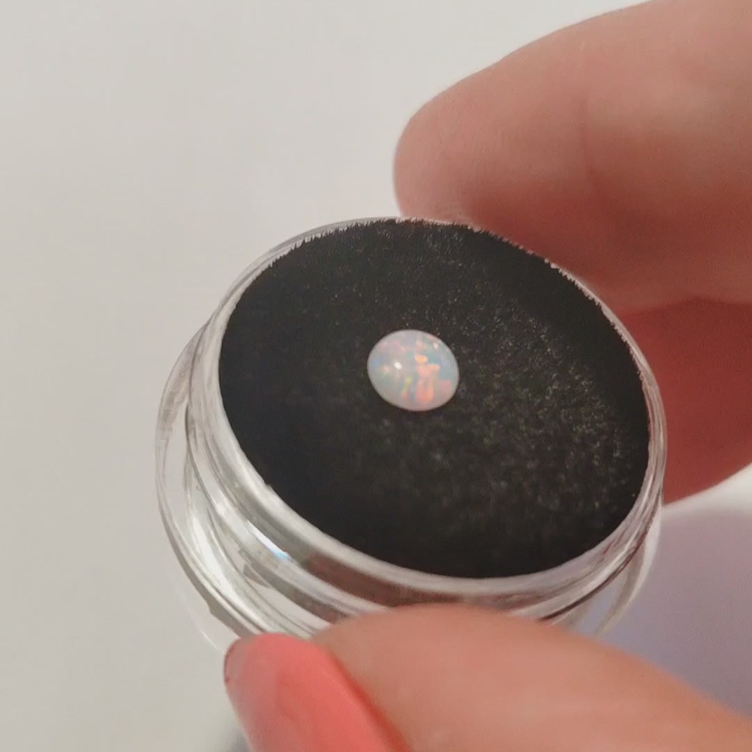 A pink opal cabochon on a jewellery cushion showing red flashes