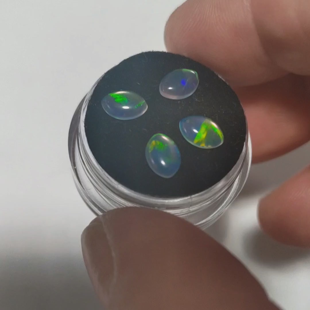 Four fireable water opals with green fire on a jewellery pot held in a hand to show the flashes of green in the opal.