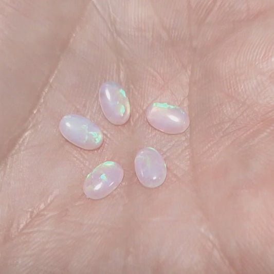 Five lab grown ovals opals white with green fire In a hand.