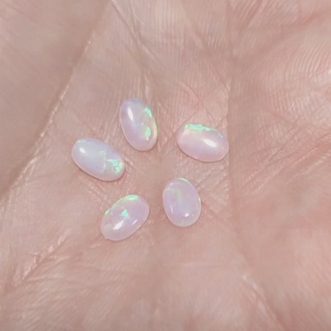 Five lab grown ovals opals white with green fire In a hand.