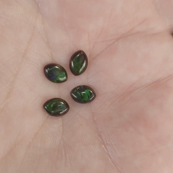 Four lab grown black opal green fire marquise opals displayed on a hand.