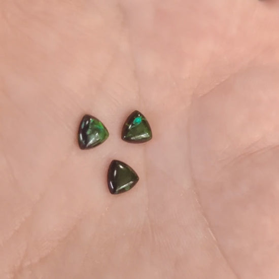 Three Lab grown Trillion black with green fire opals displayed on a hand.