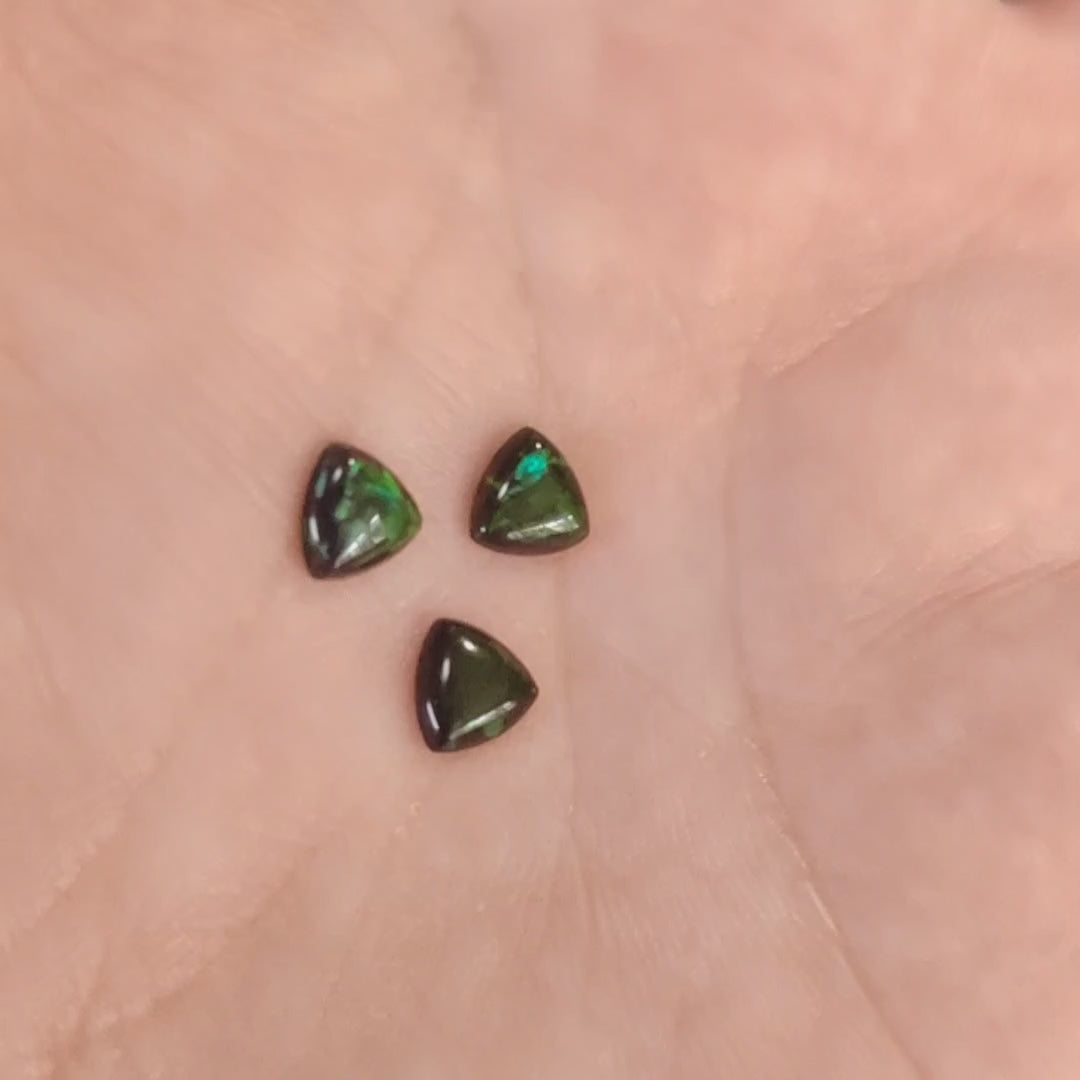 Three Lab grown Trillion black with green fire opals displayed on a hand.