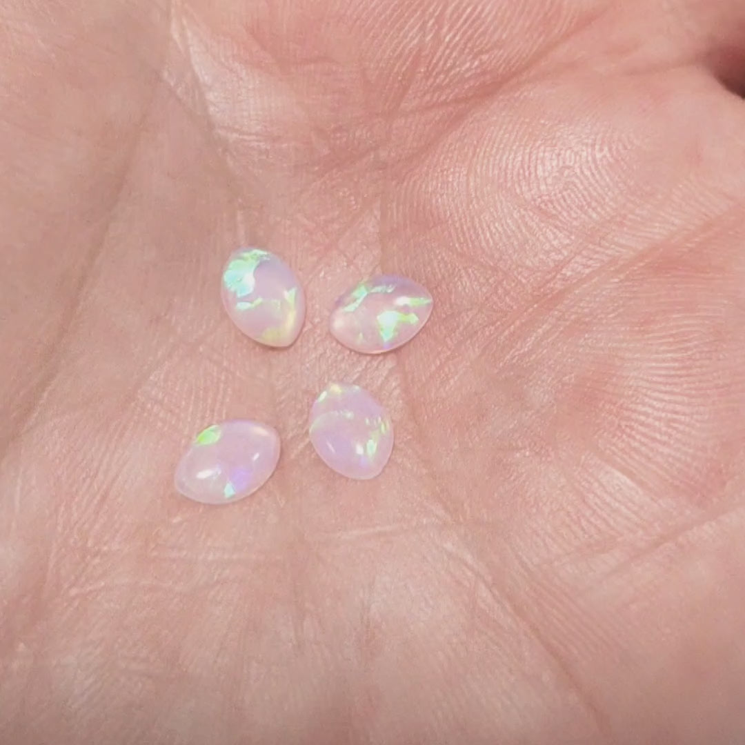 Four white opals with green fire marquise cabochons, displayed on a hand to show green flashes.