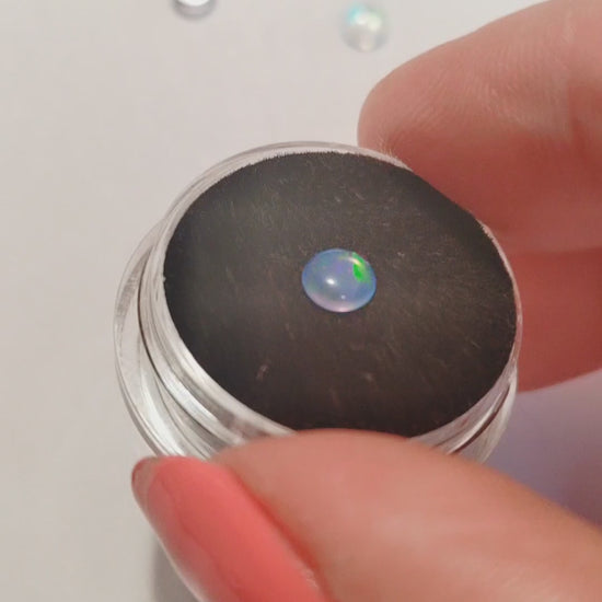 A fireable blue opal with green fire on a black jewellery mount.