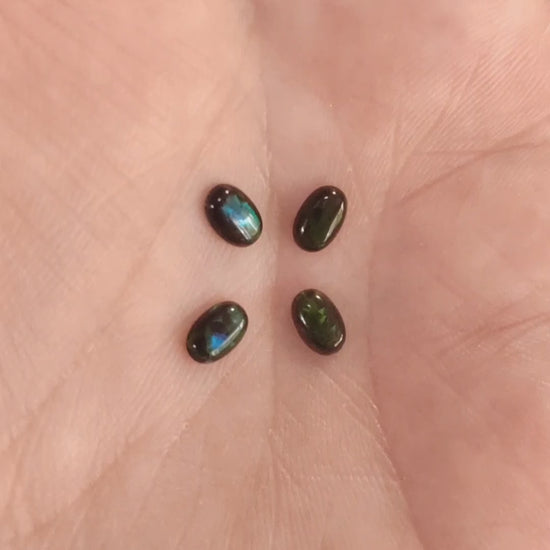 Four lab grown ovals opals black with green fire In a hand.